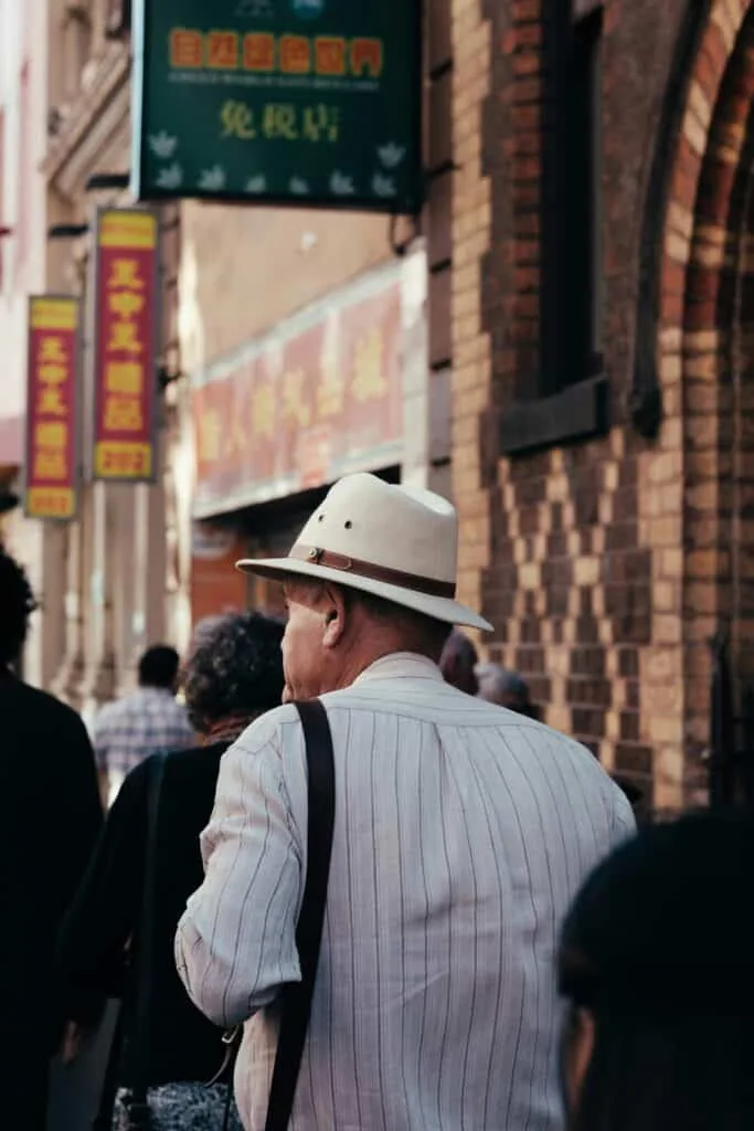 An old soul in a white hat and striped white shirt carrying a strap bag.