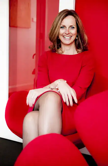 Naomi Simpson in a red dress, sitting and smiling.